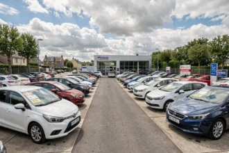 Vue large d'un grand parking de voitures d'occasion en Ille-et-Vilaine avec showroom moderne en arrière-plan